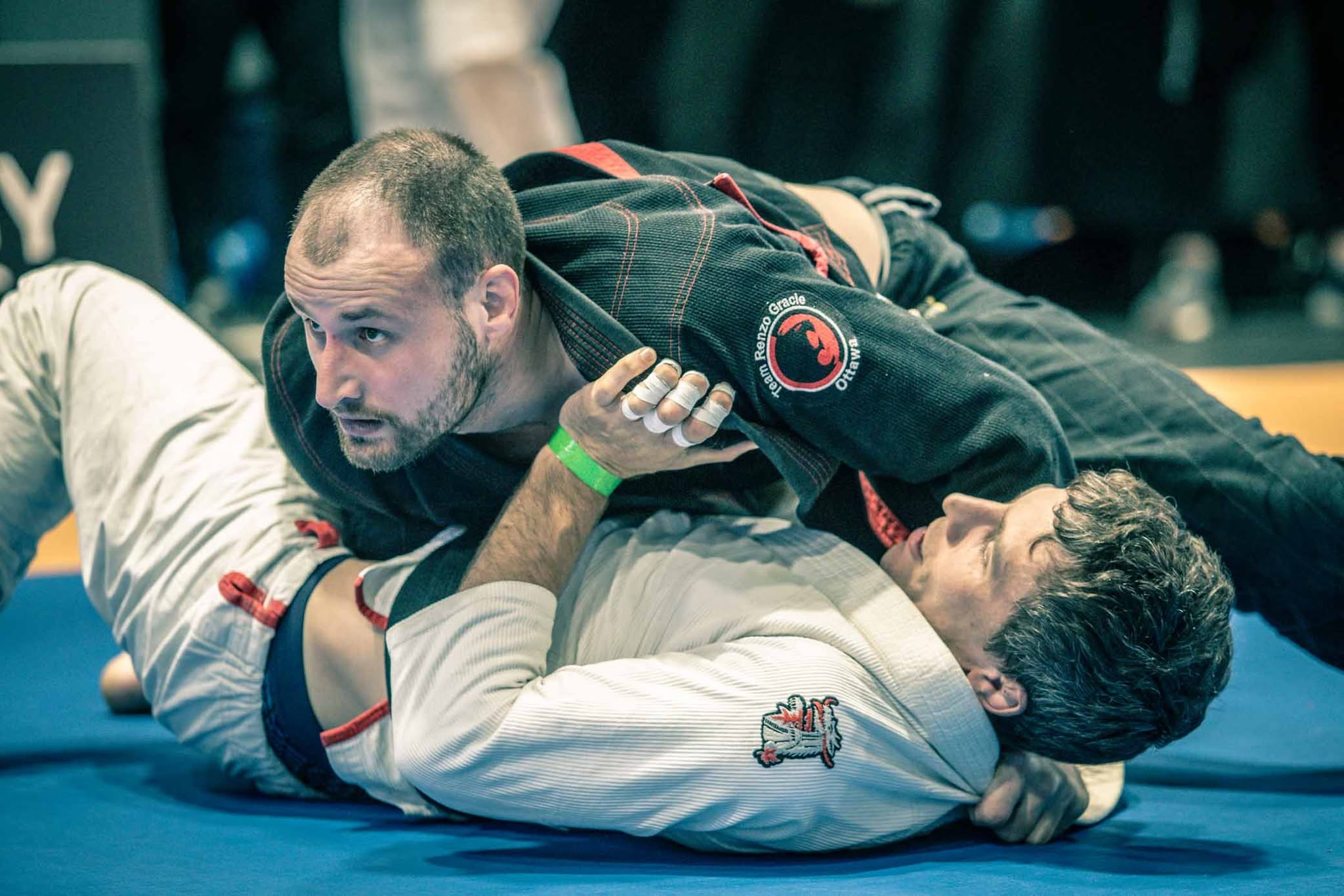 Dos adultos entrenando jiu-jitsu en el suelo, un competidor de Renzo Gracie arriba