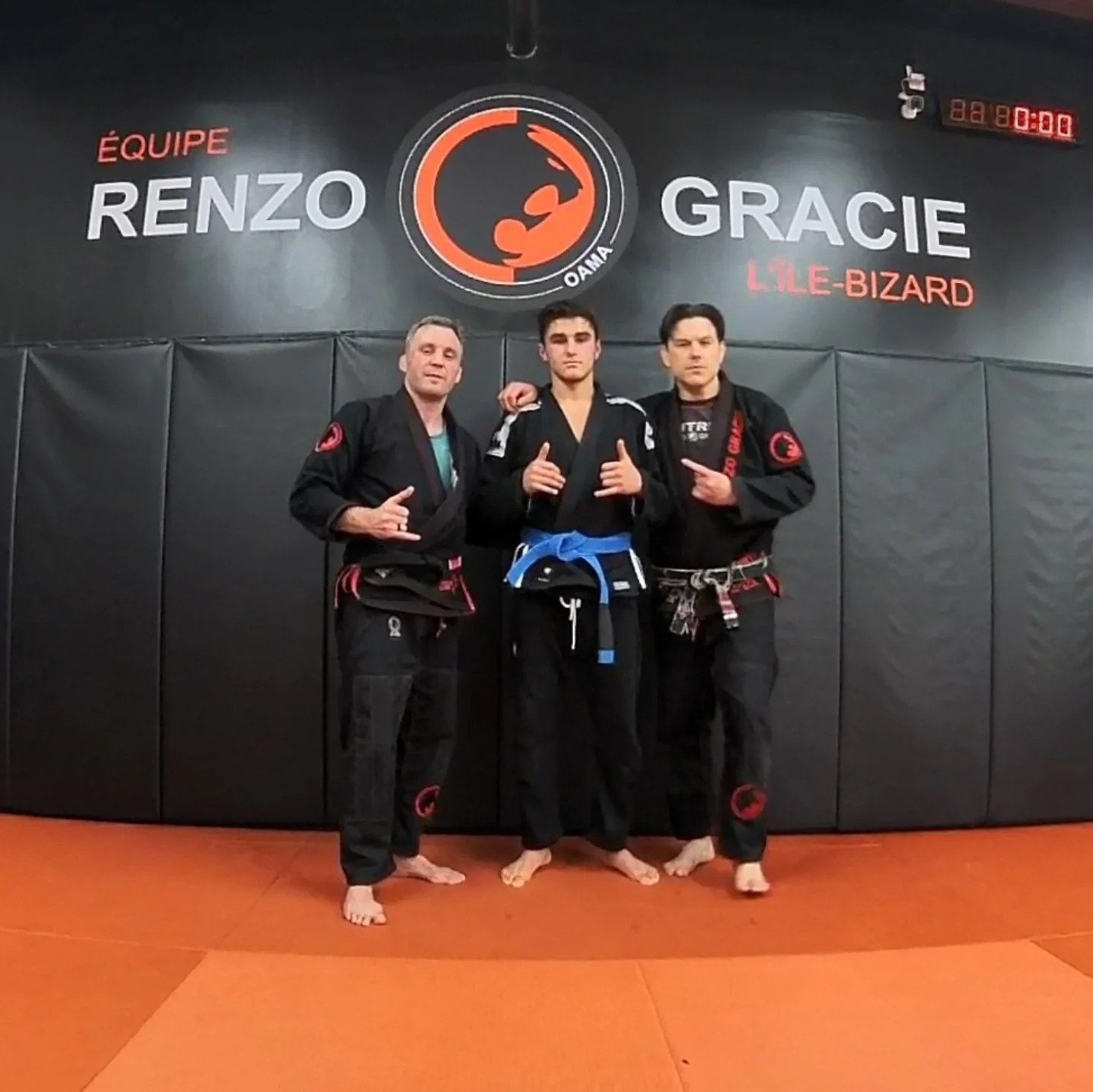 Three practitioners in black gis pose under a Renzo Gracie wall logo