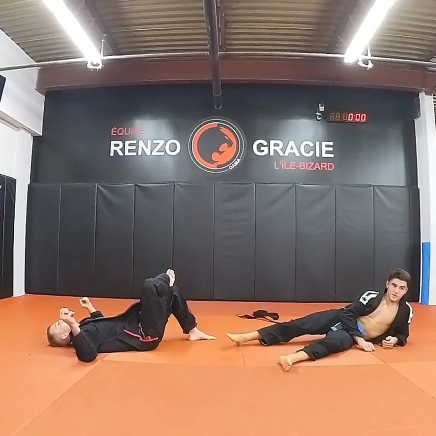 Two training partners lie on orange mats after a round