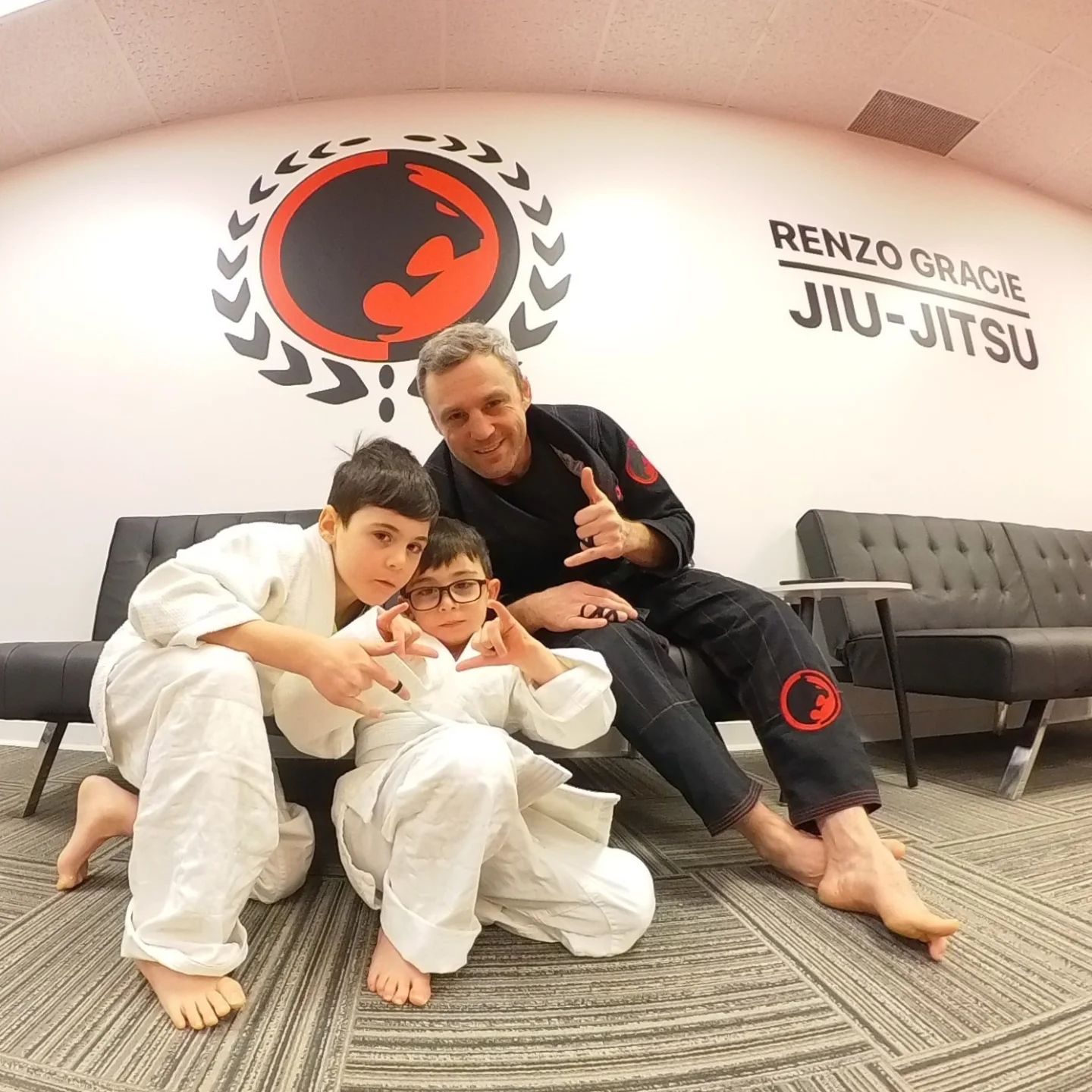 Two young students in white gis sit on the floor with their coach
