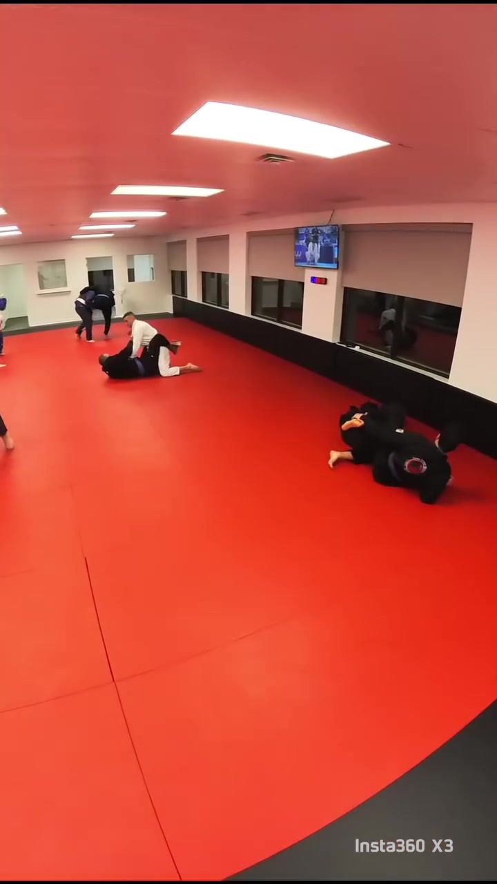 Two pairs of practitioners roll on the red mats in a wide room