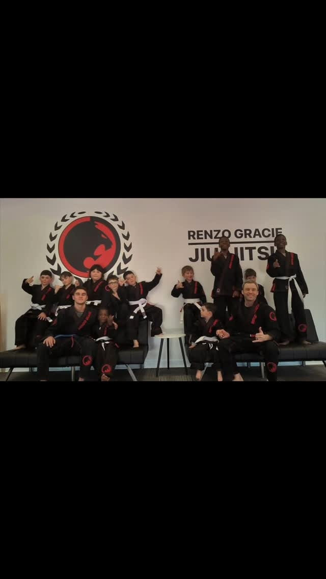 Young students and coaches in black gis pose under the academy logo