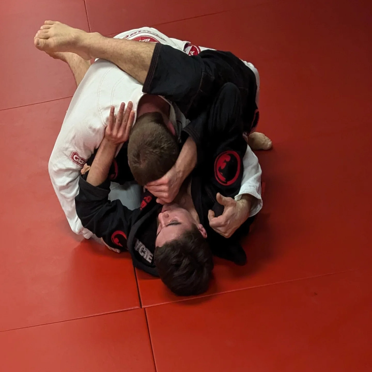 Dos compañeros con gi blanco y negro en un intercambio sobre el tatami rojo