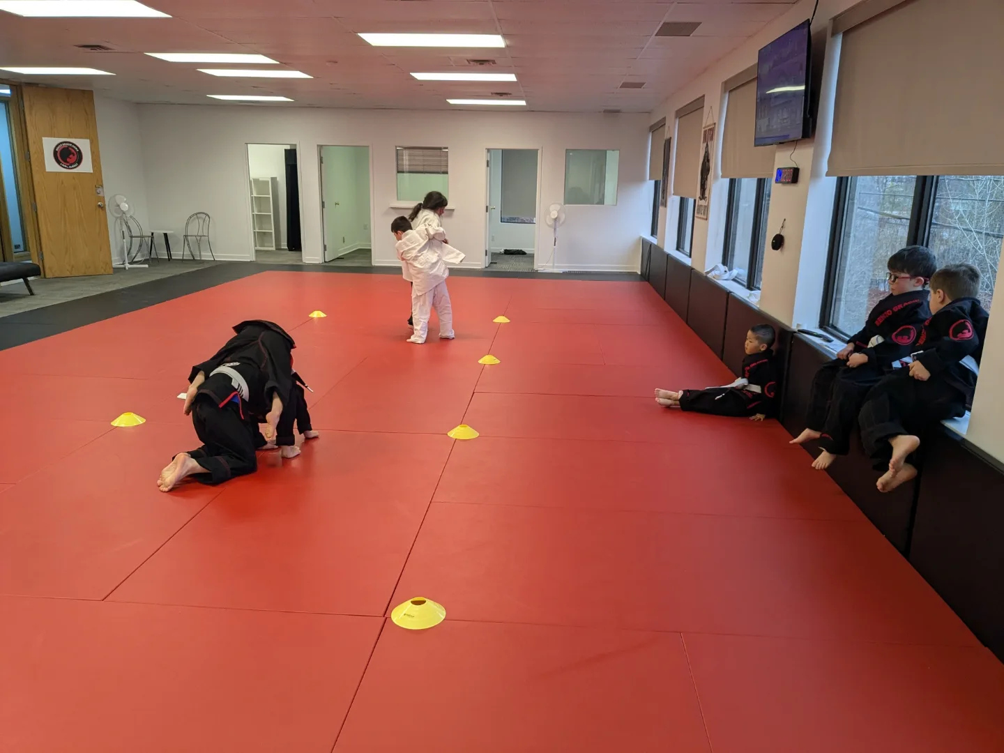 Two young students push in a sumo game while classmates sit by the windows