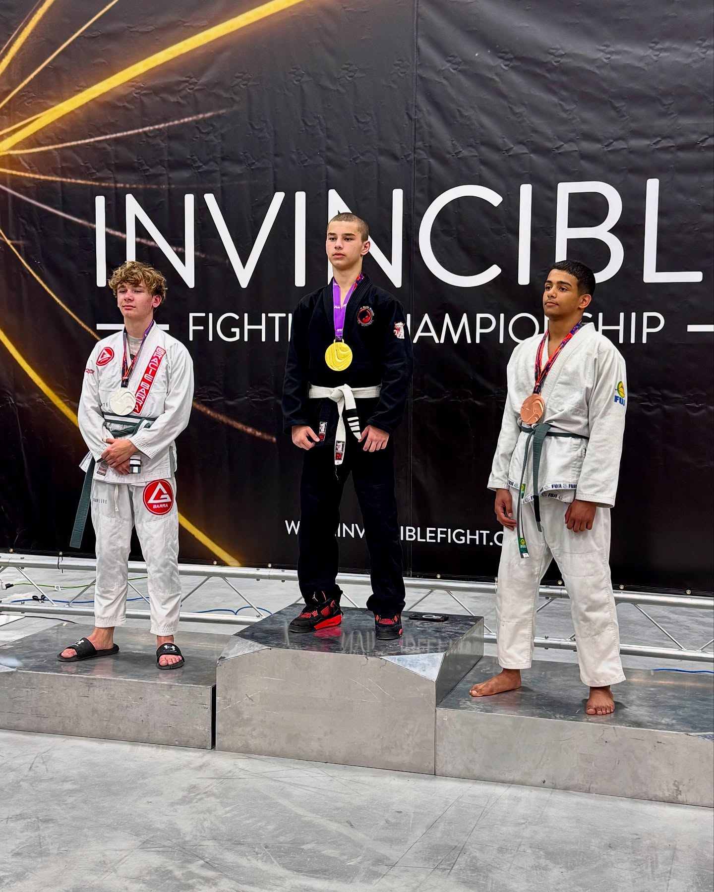 Jovens competidores com suas medalhas num pódio sob um banner do Invincible