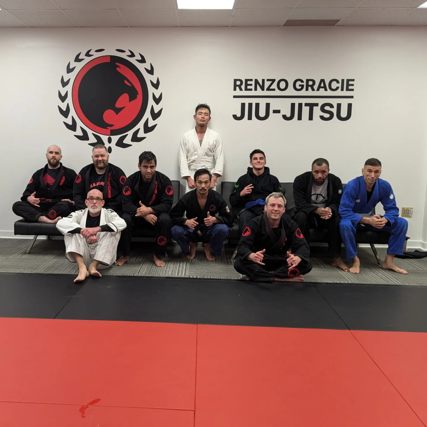 A training group in gis poses under the academy logo on red mats