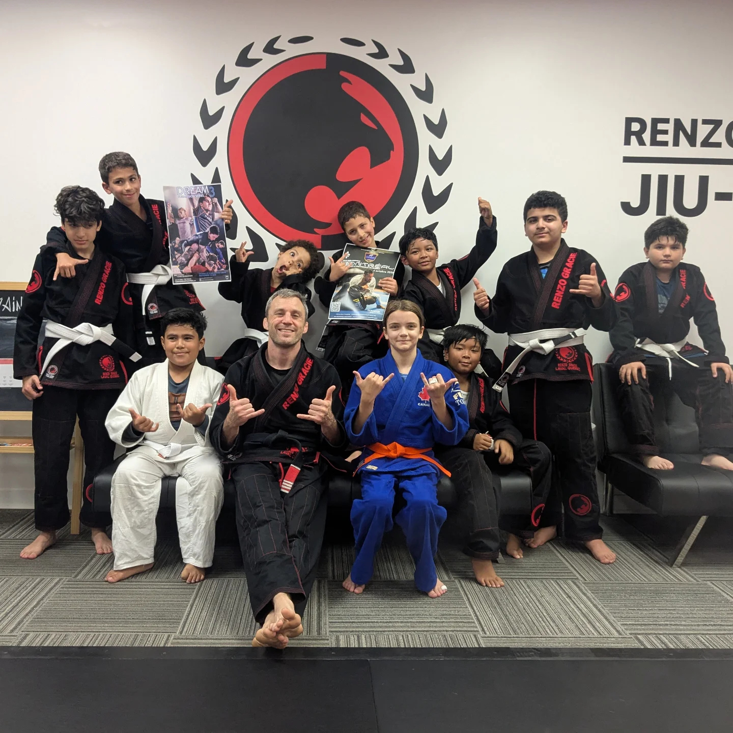 Junior students in gis and a coach pose under the academy logo, two of them holding event posters