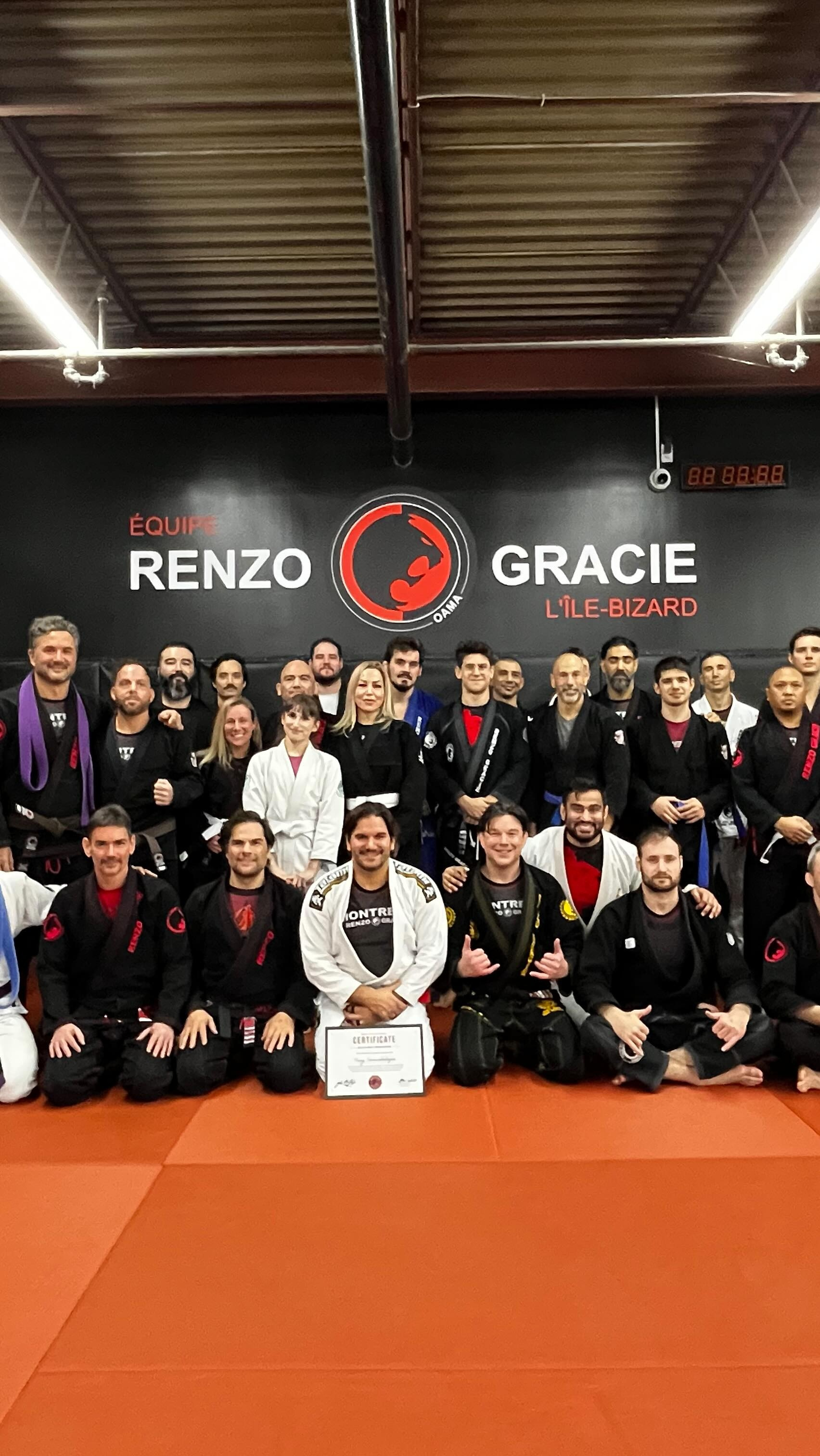 Un gran grupo posa sobre tatami naranja bajo el letrero de Renzo Gracie Île-Bizard