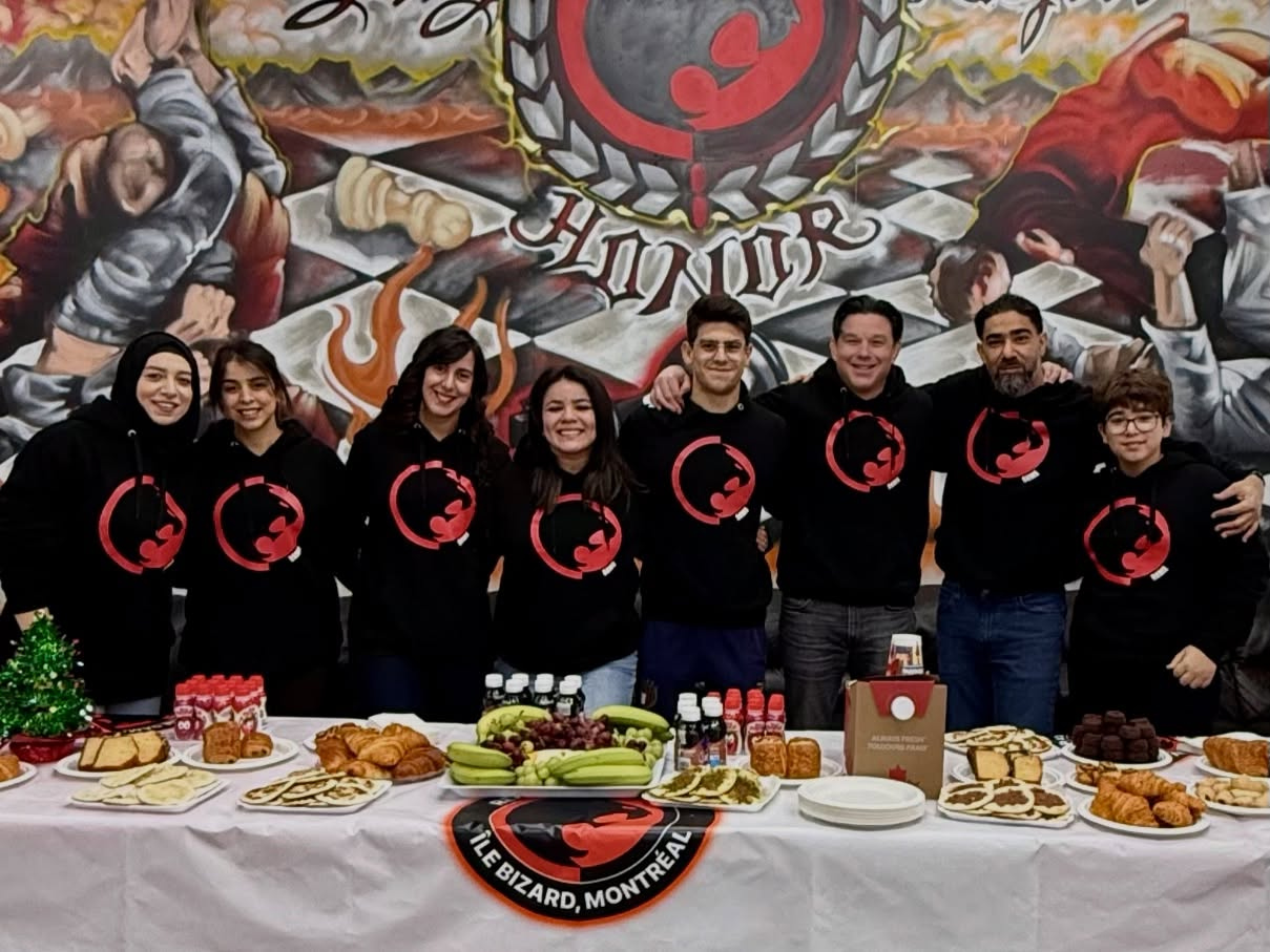 Staff in black team hoodies stand behind a holiday buffet in front of a mural