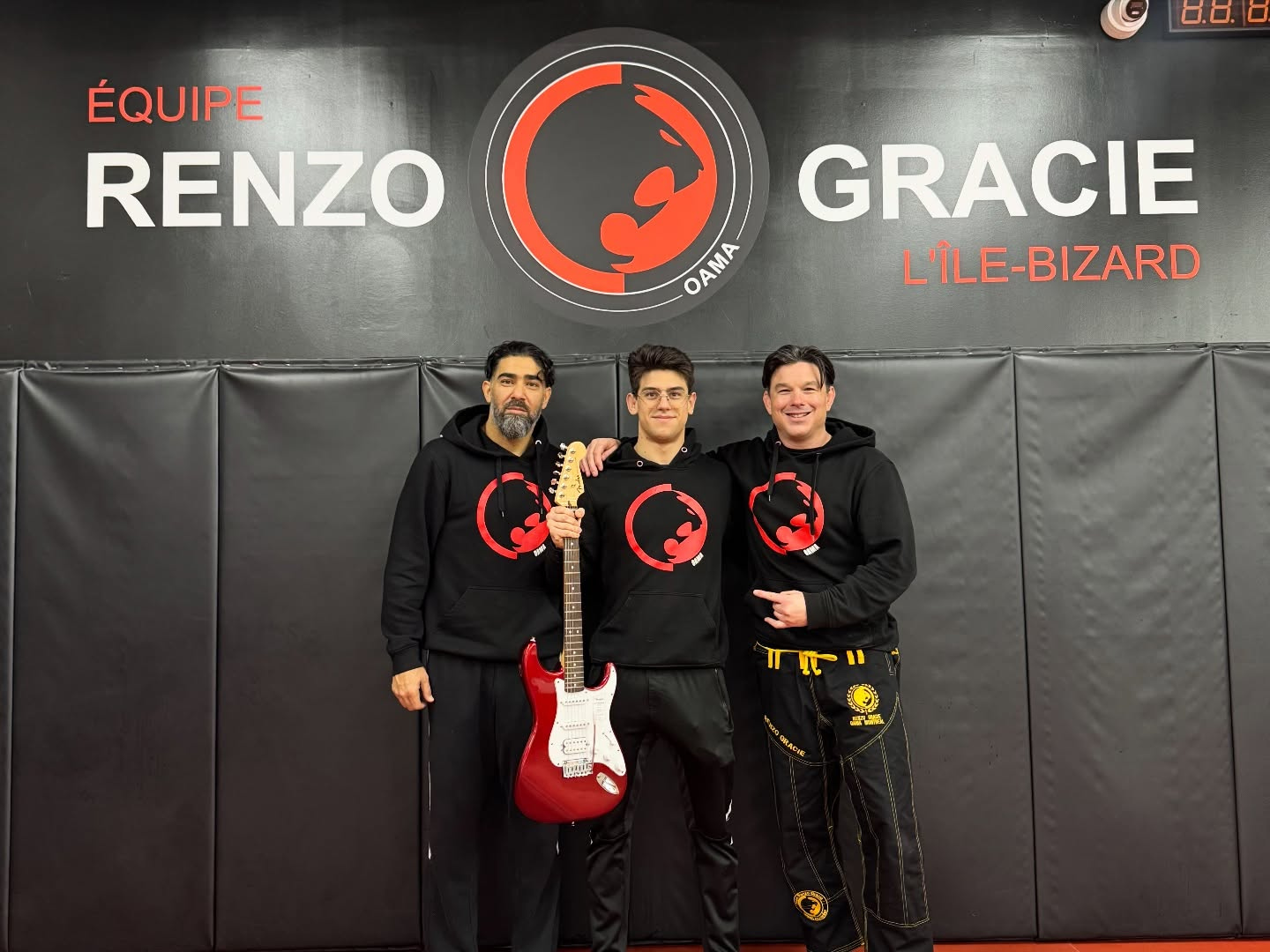 Three people in black team hoodies pose with a red electric guitar