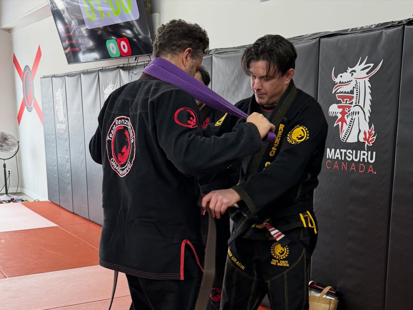 A coach ties a purple belt around a student's waist