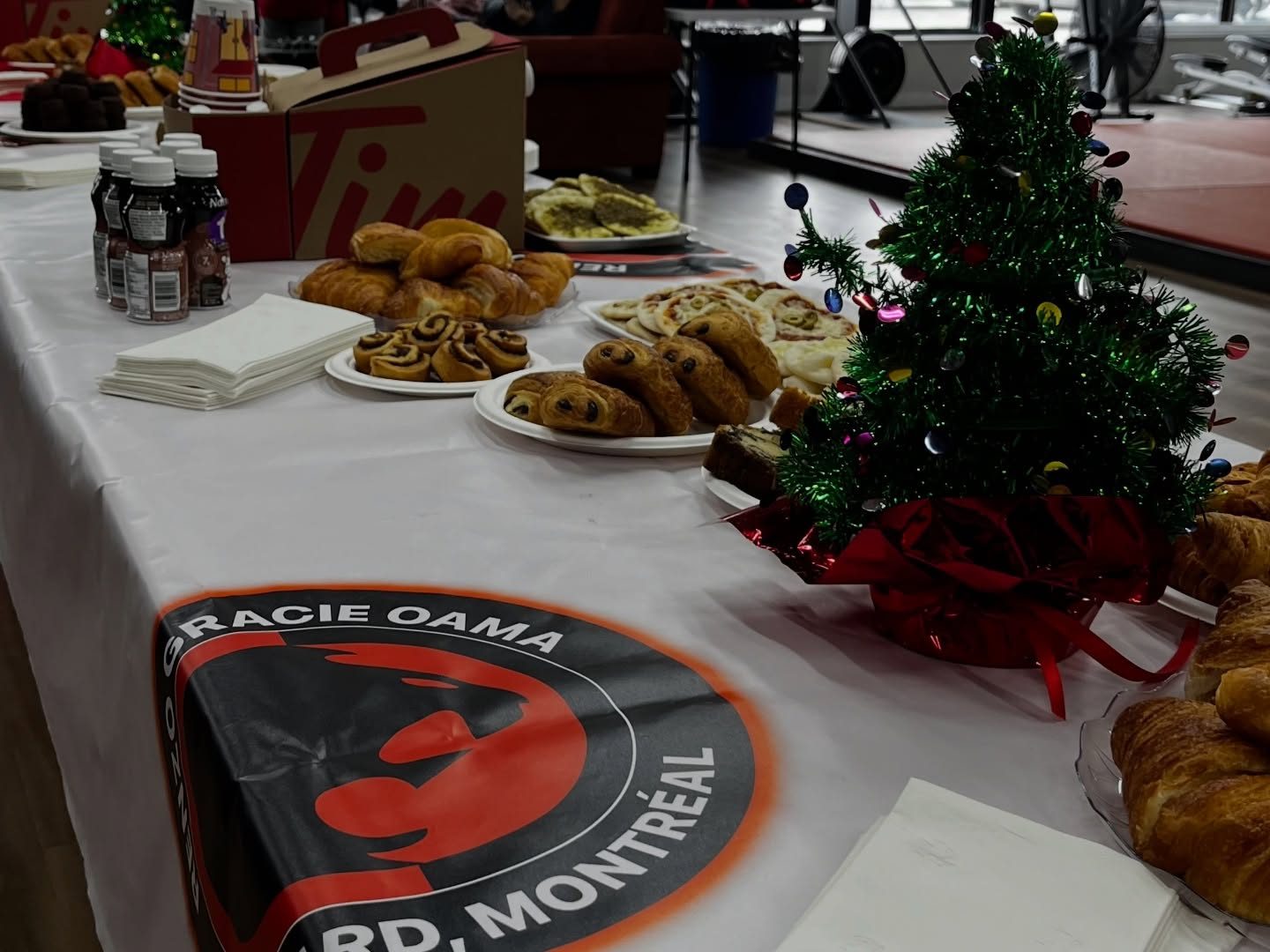 A holiday buffet with pastries and a small decorated tree on a Renzo Gracie banner