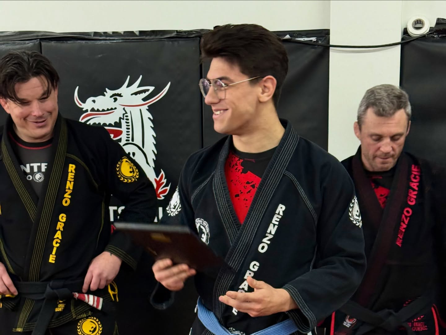 Three people in black gis smile as one holds an award