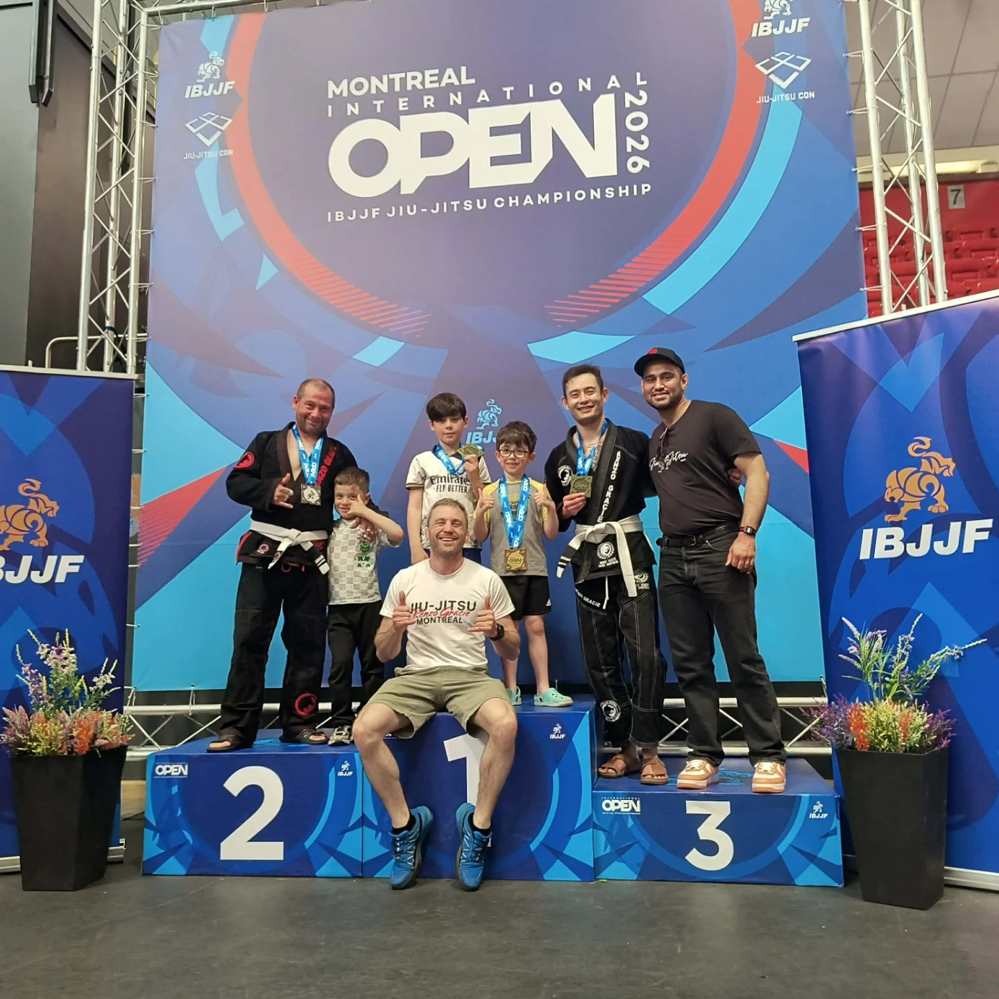 Des membres de l'équipe et des proches réunis sur un podium numéroté de l'IBJJF sous la bannière de l'Open de Montréal
