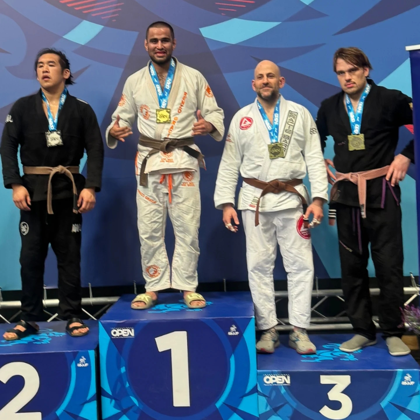 Quatre compétiteurs adultes en kimono blanc et noir sur le podium avec leurs médailles