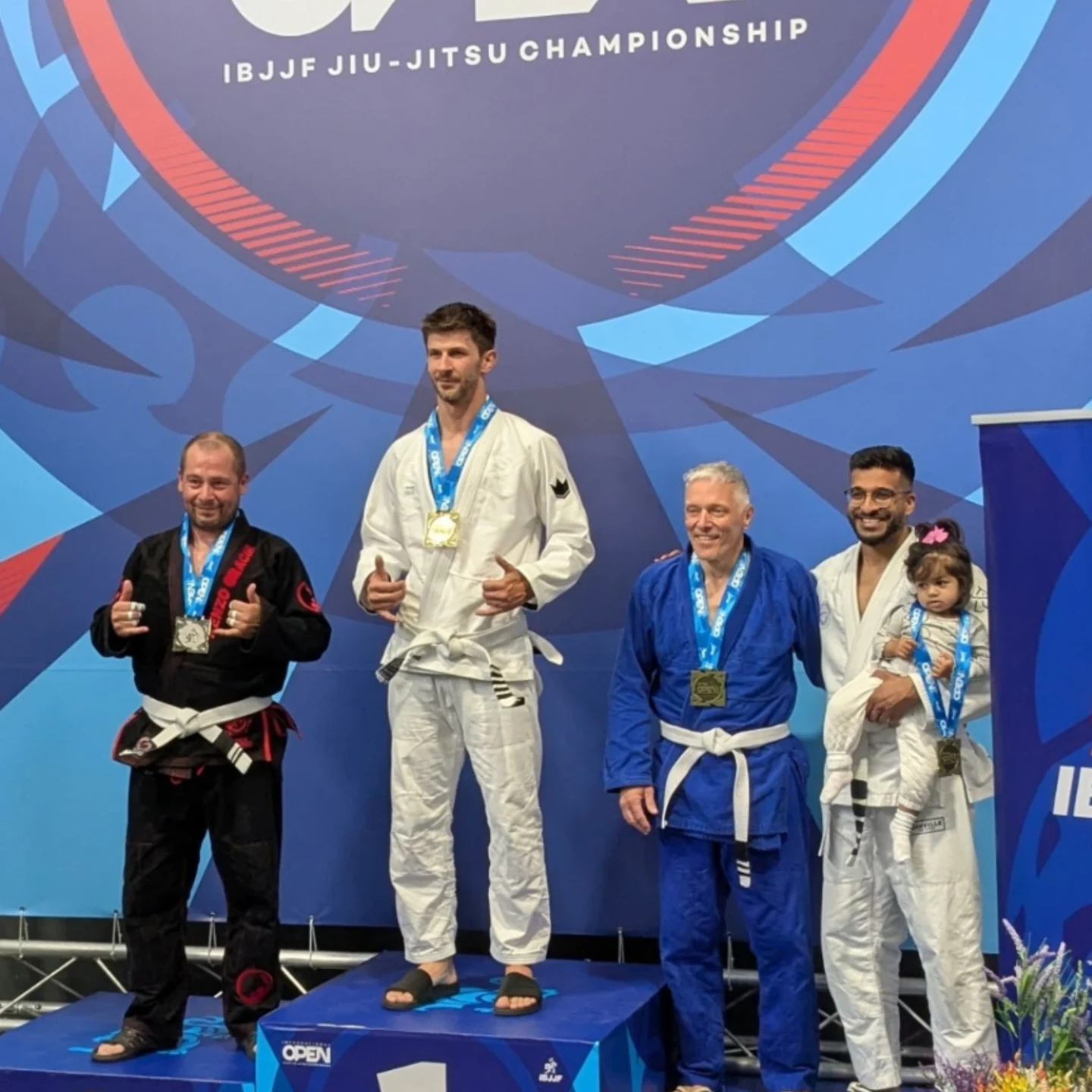 Des compétiteurs en kimono noir, blanc et bleu sur le podium avec leurs médailles