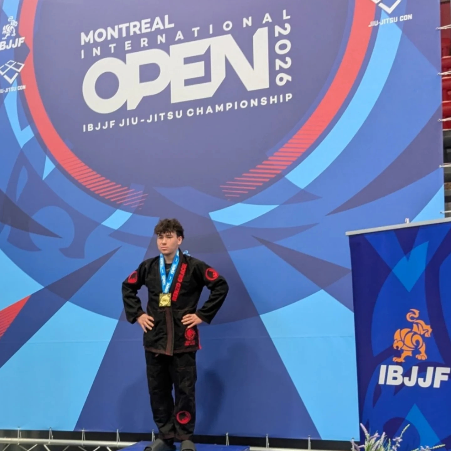 Un compétiteur en kimono noir avec sa médaille sous la bannière de l'Open de Montréal