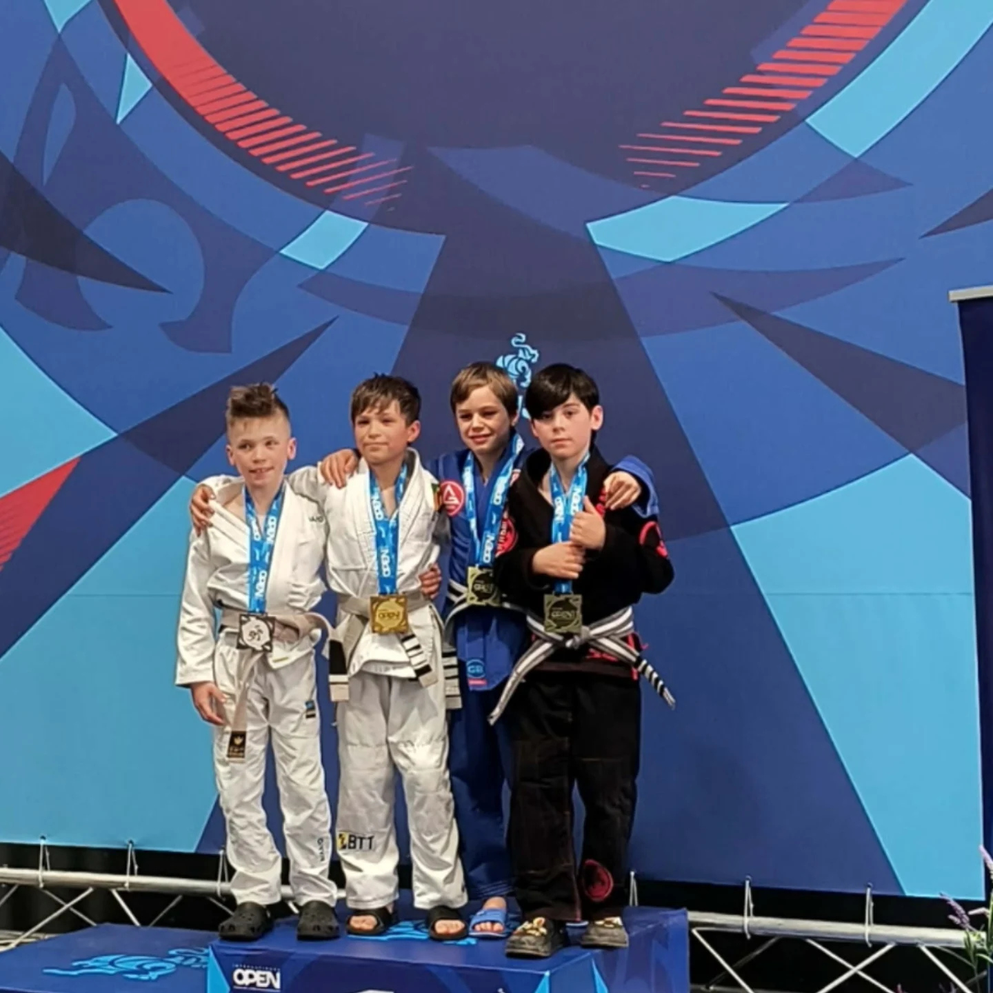 Quatre jeunes compétiteurs en kimono blanc et noir côte à côte avec leurs médailles