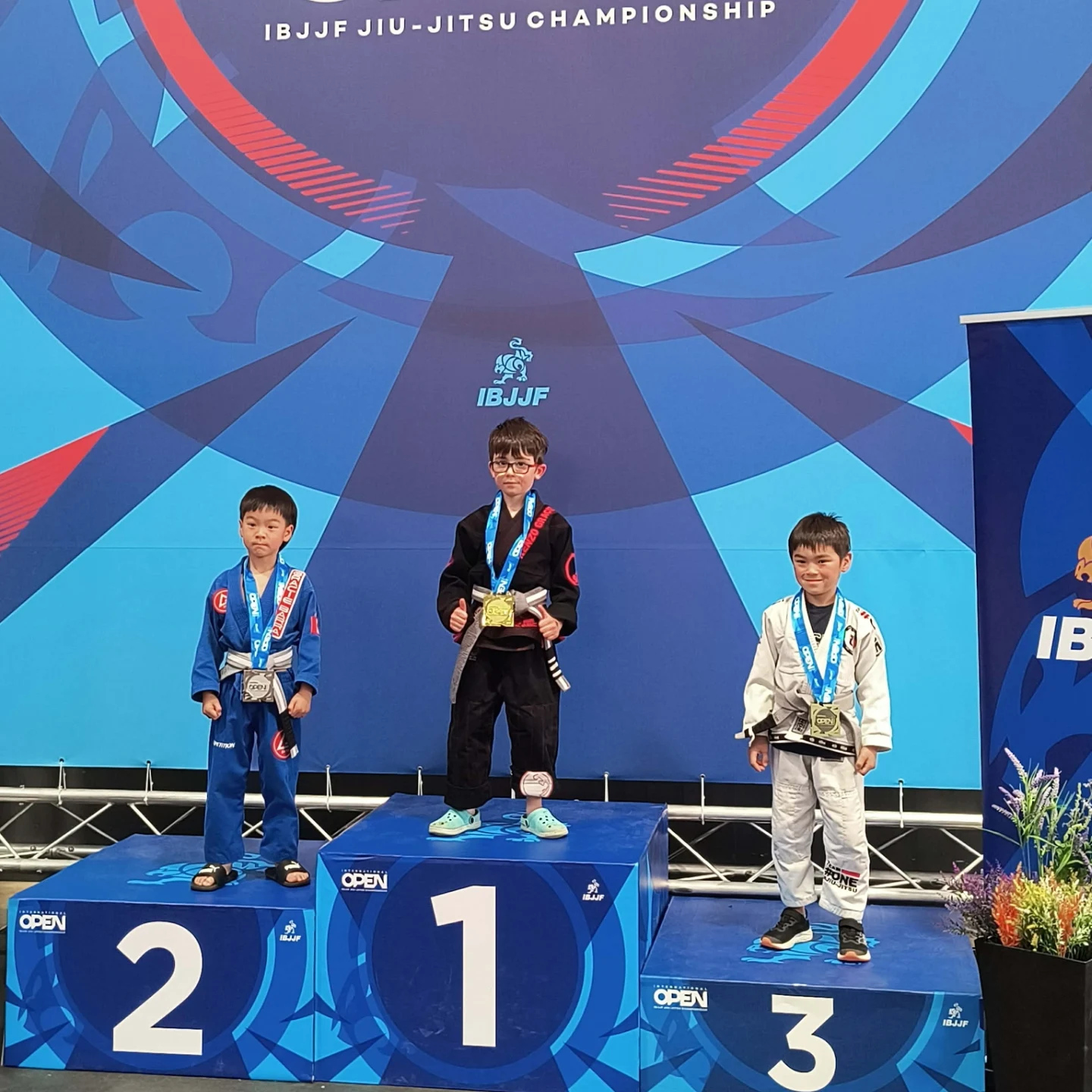 Trois jeunes compétiteurs sur le podium enfants numéroté avec leurs médailles