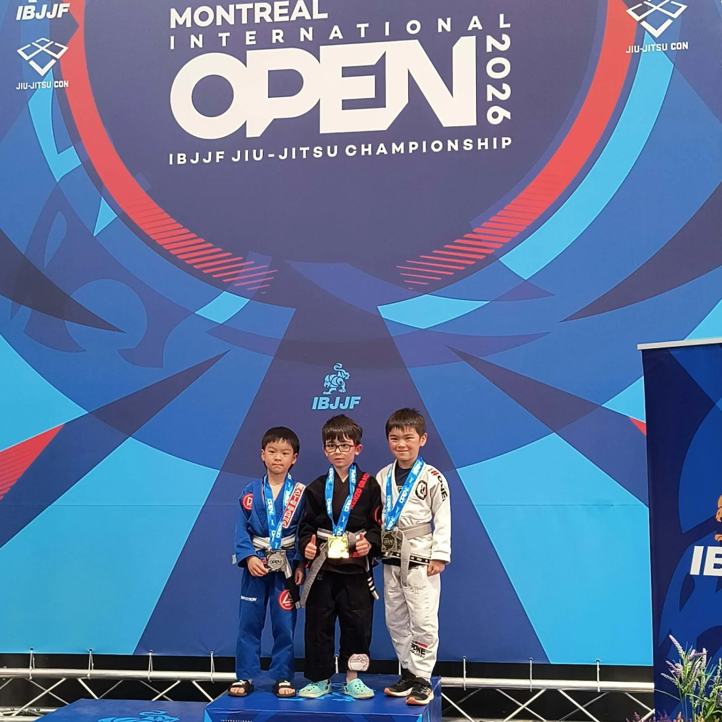 Trois jeunes compétiteurs en kimono portent leur médaille sous la bannière de l'Open de Montréal