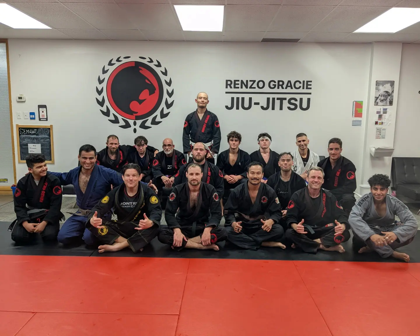 A turma de adultos de kimono preto reunida no tatame sob o letreiro Renzo Gracie Jiu-Jitsu