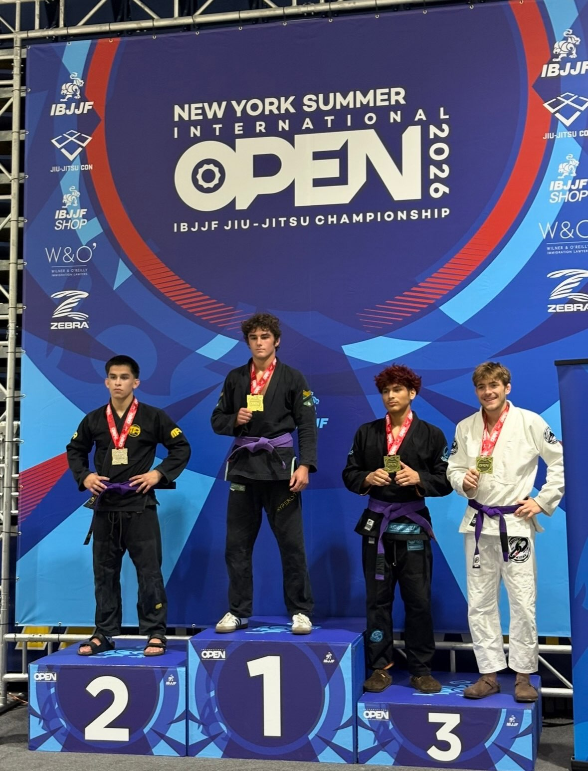 Des compétiteurs ceinture violette en kimono noir et blanc sur le podium avec leurs médailles