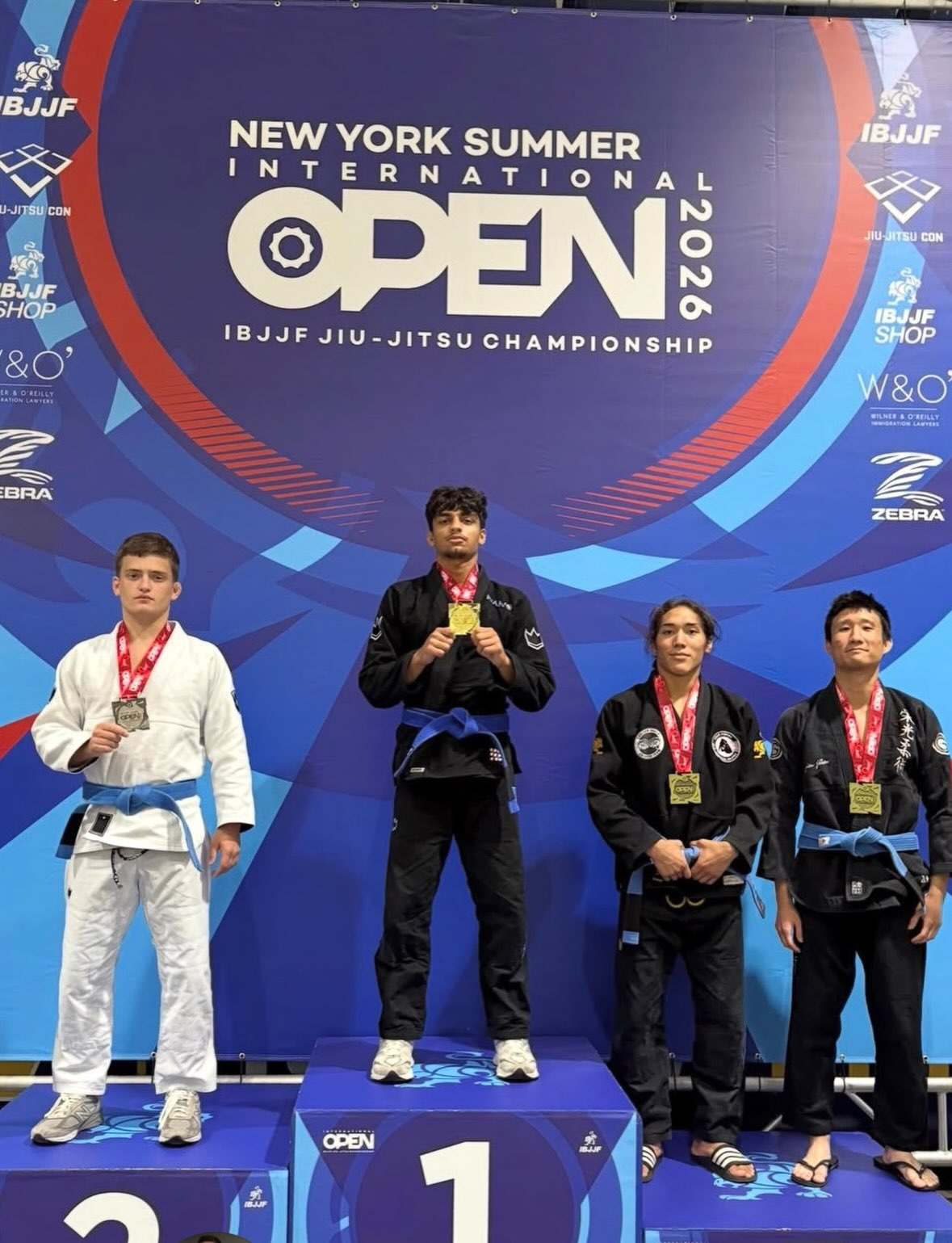 Des compétiteurs ceinture bleue sur le podium avec leurs médailles sous la bannière New York Summer Open