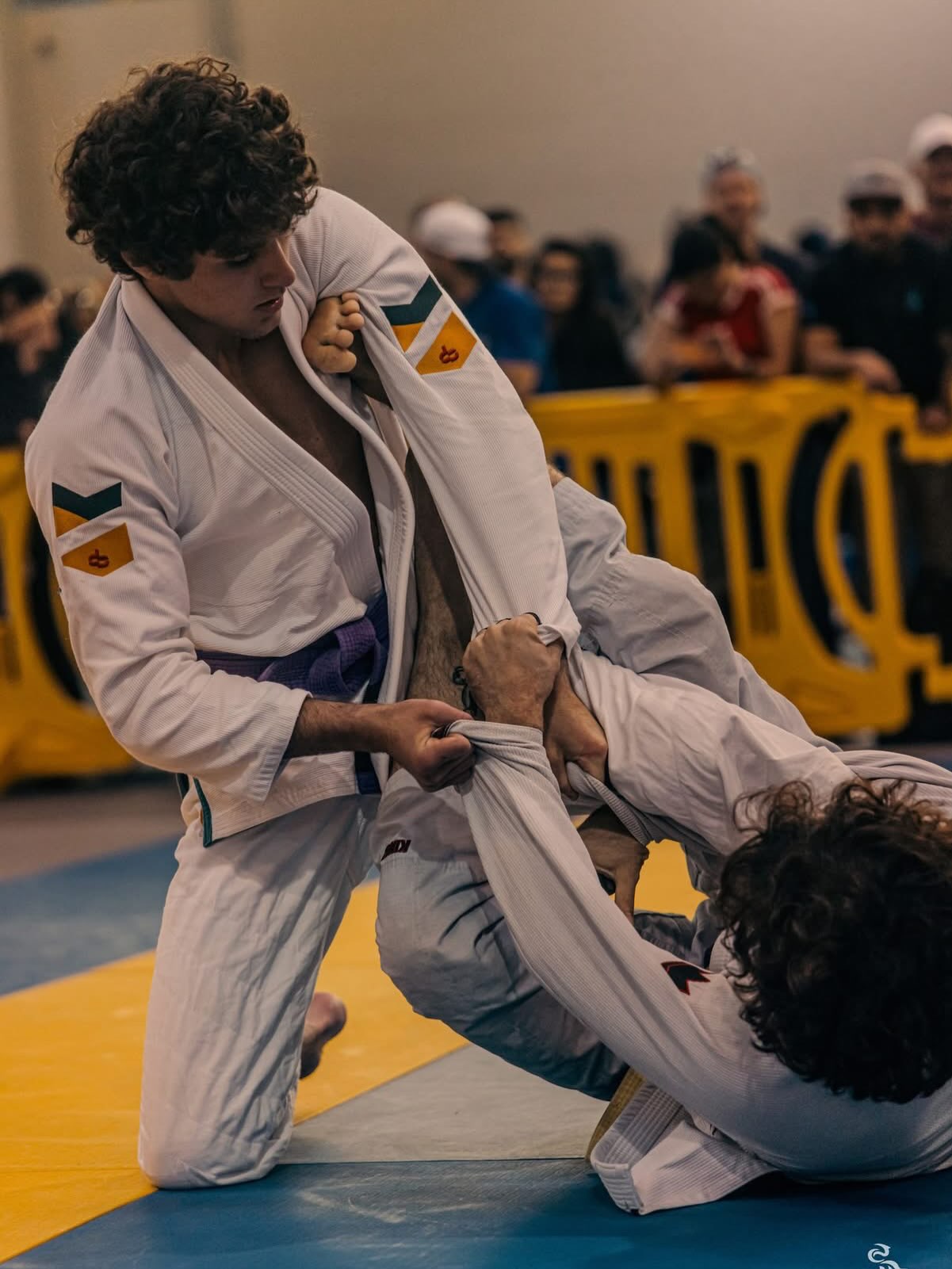 Dos competidores se agarran del gi durante un combate de cinturones morados